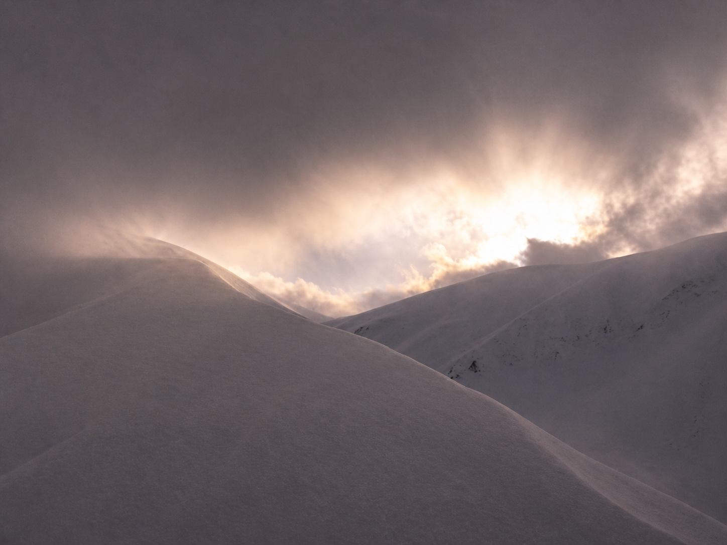Sun breaking through clouds over snow-covered hills